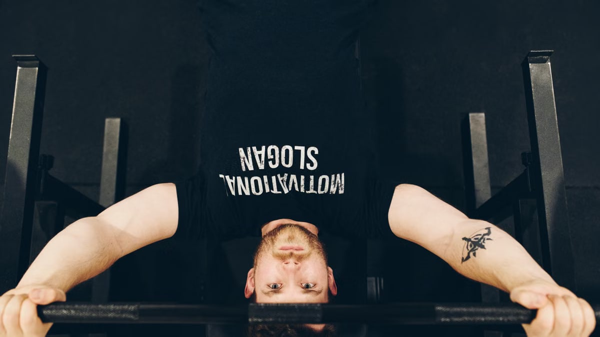 Bearded sportsman in t shirt with inscription exercising with weight while looking at camera